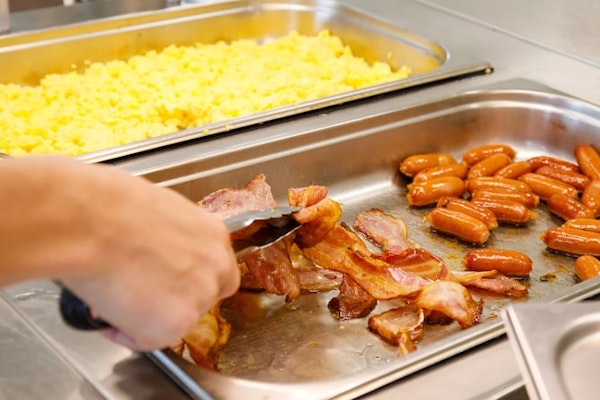 A person is selecting bacon from the breakfast buffet area, which also included sausages and scrambled eggs at Hotel Laugar Reyk