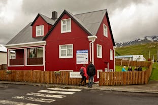 An exterior view of the red house at Grundarfjordur HI Hostel with people walking through the gate to the reception area, others