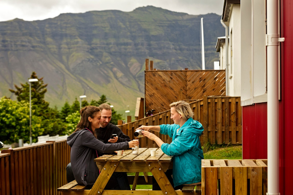 People are pouring tea and relaxing on a picnic bench on the grassy area outside Grundarfjordur HI Hostel with the mountains tow