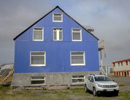 The blue exterior of Thorshofn HI Hostel in Northeast Iceland with a car parked in front on a grey day.