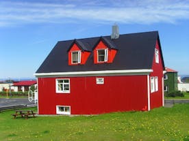 Zewnętrzny widok na czerwony dom hostelu Grundarfjordur HI ze stołem piknikowym na trawie.