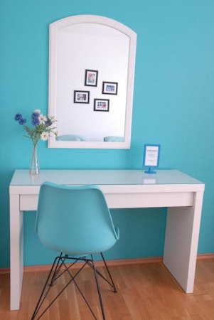 A light blue chair and walls and a white table with a vase of flowers and a mirror above at Grundarfjordur HI Hostel.