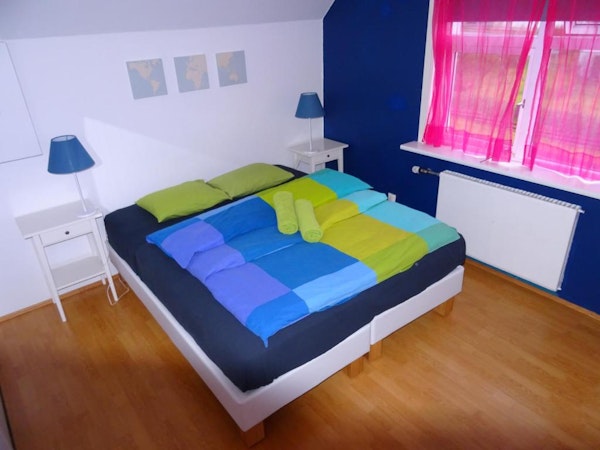 An interior birdseye view of a double room at Grundarfjordur HI Hostel with a bed, bedding, towels, bedside tables, and lamps.