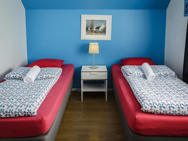 A twin room at Grundarfjordur HI Hostel with beds, bedding, towels, a bedside table, lamp, and artwork on the wall.
