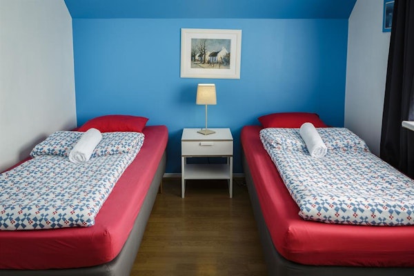 A twin room at Grundarfjordur HI Hostel with beds, bedding, towels, a bedside table, lamp, and artwork on the wall.