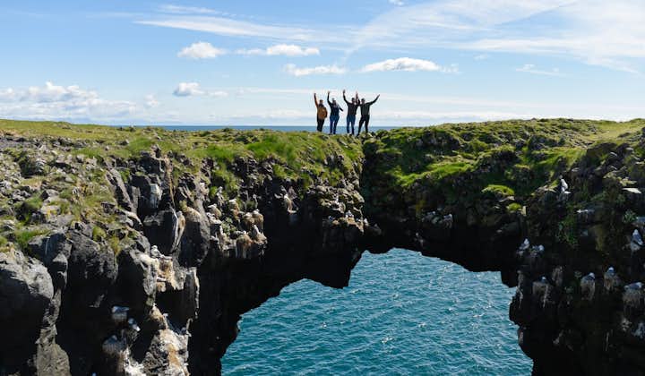 Cuatro personas posan encima de las espectaculares formaciones de un acantilado en Arnarstapi con sus brazos al aire.