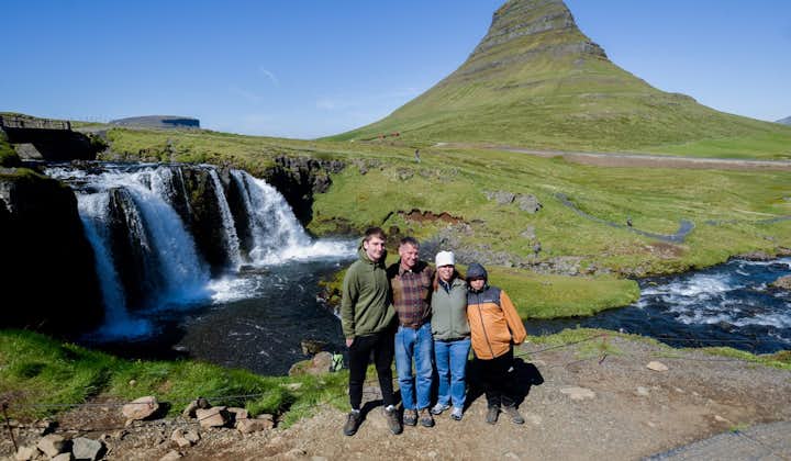 Een familie van vier personen staat voor de berg en waterval van Kirkjufell.