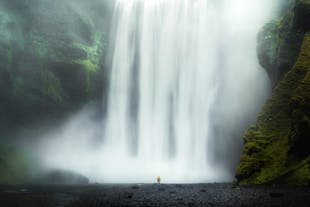 A person stands in front of the massive Skogafoss waterfall in Iceland.