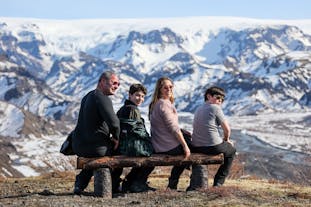 A smiling family sits on a bench with the snowy mountains surrounding Thorsmork in the background.