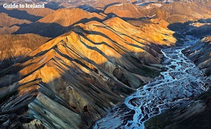 A bird's eye view of Landmannalaugar shows the picture-perfect contrasts of the sun shining over caramel-colored mountain peaks and glacial rivers weaving through the valley below.