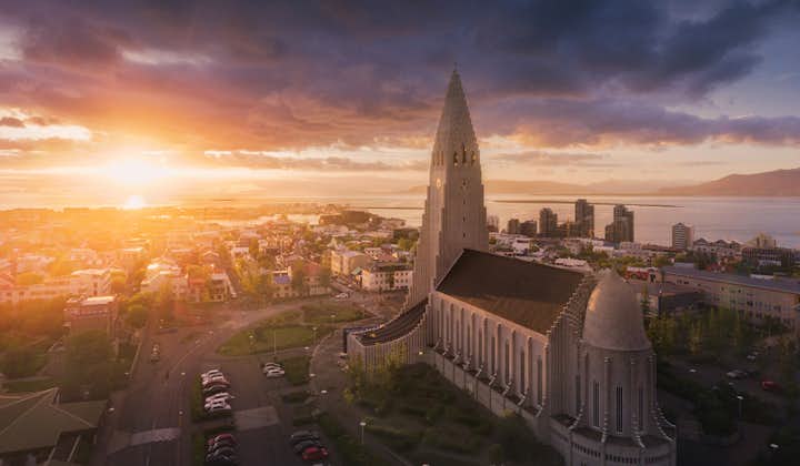 An overhead view of Reykjavik city at sunset with Hallgrimskirkja church as its centerpiece and the sky colored in shades of orange, pink, blue, and purple.