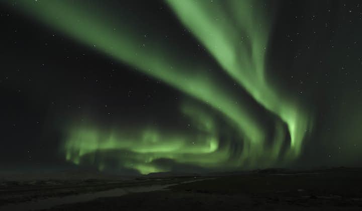The aurora borealis lights up the starry winter sky in splashes of green.