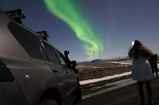 A participant on this private aurora borealis tour takes a photo of the northern lights next to an SUV.