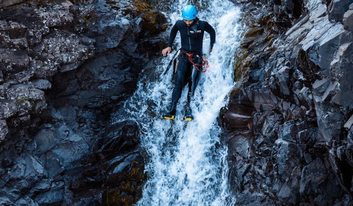 A person uses a waterfall as a slide on this thrilling canyoning tour in Southeast Iceland.