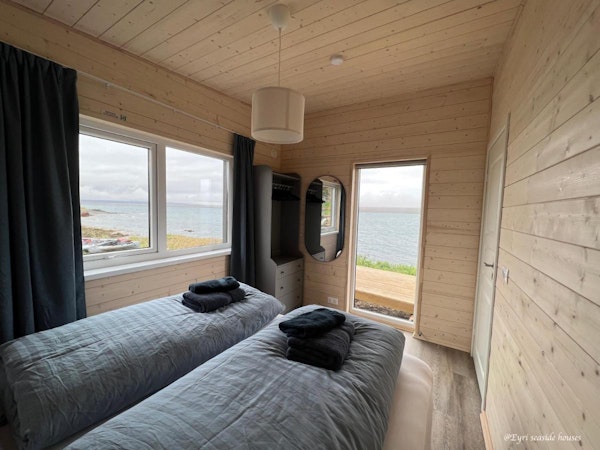 A modern twin bedroom with towels, linen, a closet, and an amazing sea view out the window at Eyri Seaside Houses in Northwest I
