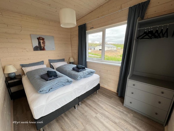 A modern double bedroom with towels, linen, a closet, and lovely countryside views out the window at Eyri Seaside Houses in Nort