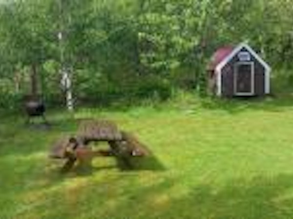 The cabin is surrounded by forest and a large, peaceful garden with a picnic table.