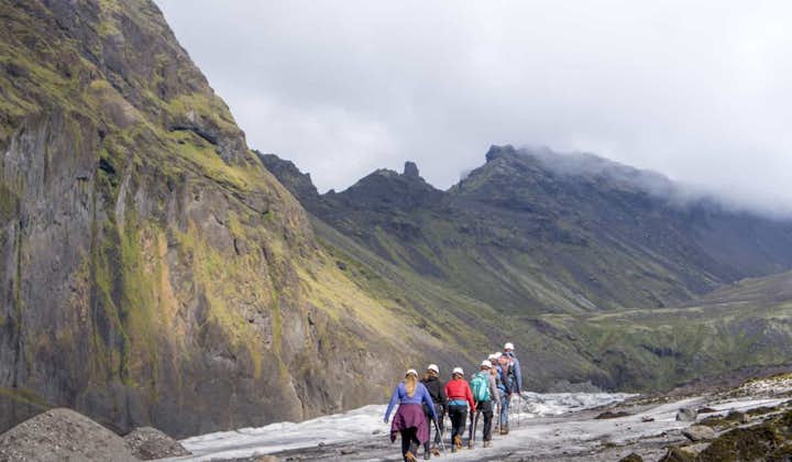 People walk up the Falljokull outlet glacier in a line, with mountains towering beside them.