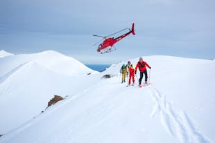Three people skiing with a helicopter taking off behind them on a mountain in North Iceland.
