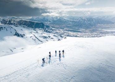 A group of heliskiers walking along some fresh mountain snow in the Troll Peninsula.