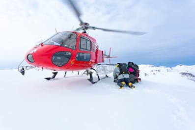 Two people prepare their heliskiing equipment at the side of a helicopter on the Icelandic slopes.