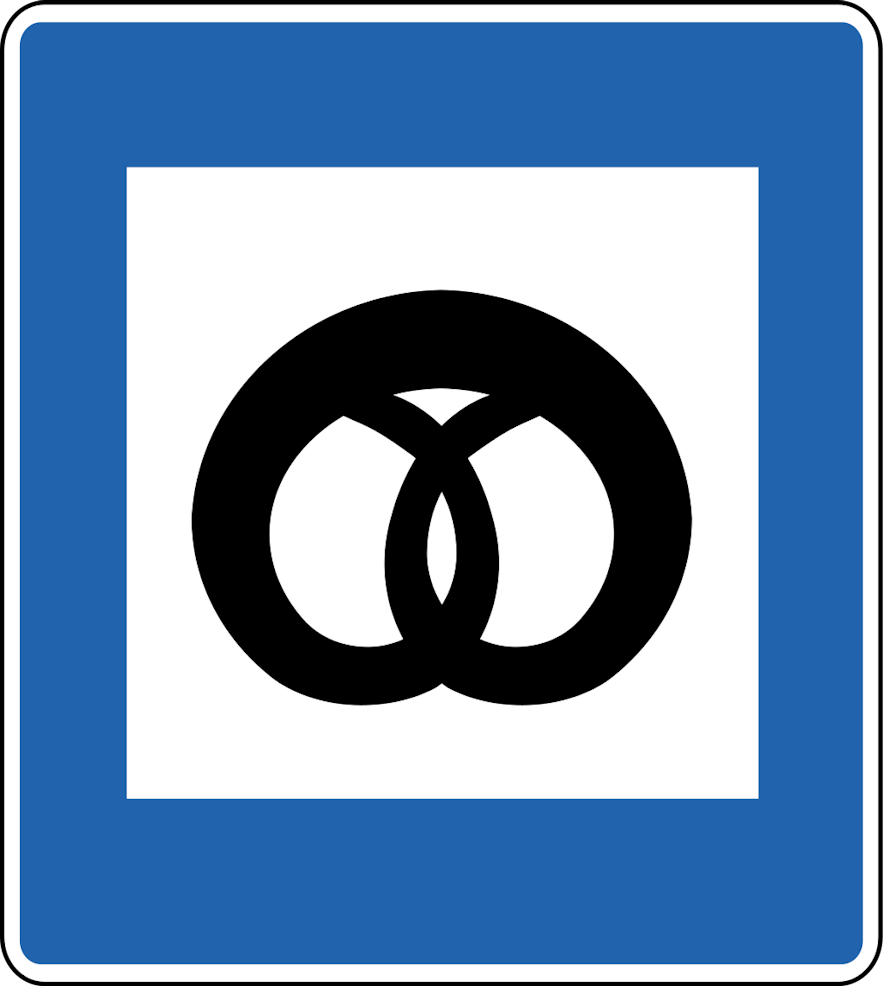 A blue and white square road sign in Iceland with a black image of a pretzel, indicating a bakery.