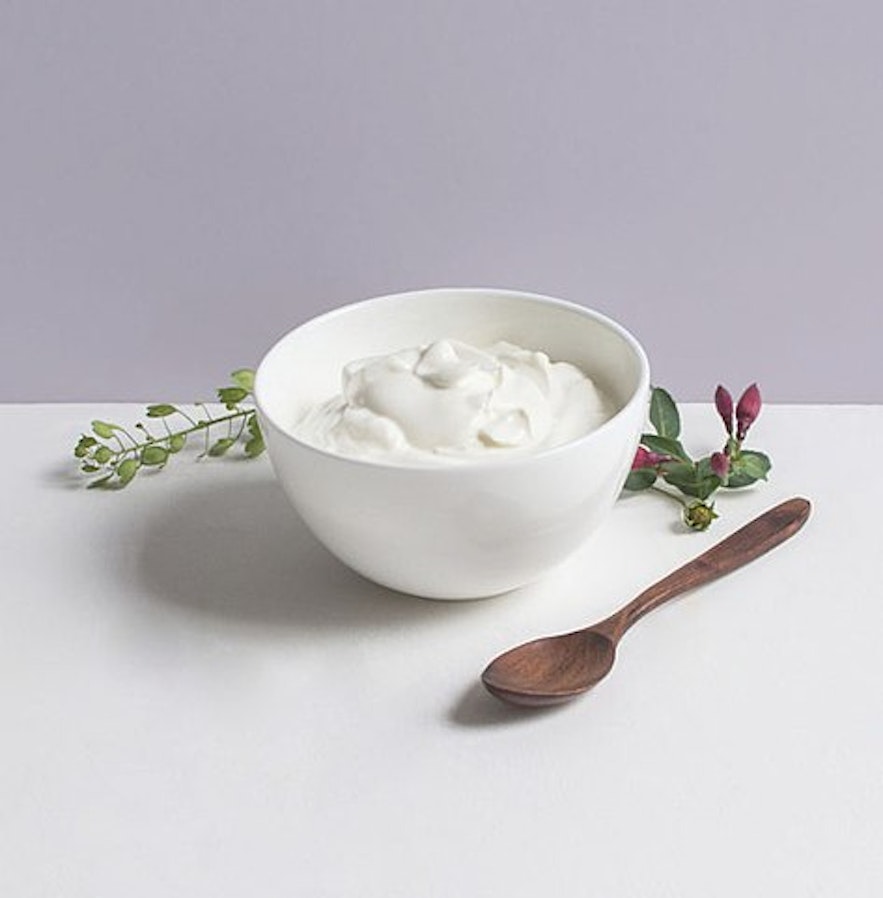 A white bowl full of skyr and a small wooden spoon next to it.