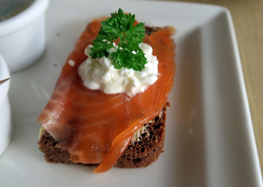 Rye bread topped with smoked salmon, skyr, and fresh herbs on a plate.