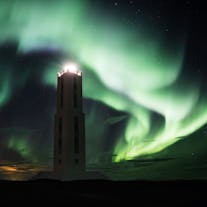 A lighthouse surrounded by the large green swirls of the northern lights above.