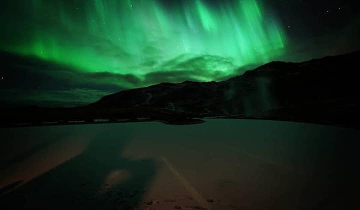 The aurora borealis produces a dazzling display of green in the night sky above the mountains.