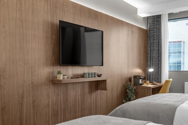 A flat-screen TV mounted on a wall with a shelf underneath it in one of the rooms at Alva Hotel.
