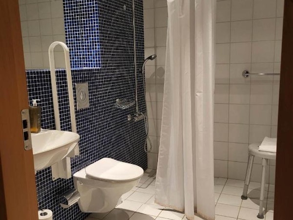 An accessible bathroom at Dala Hotel with a shower, stool, and grab rails next to the toilet.
