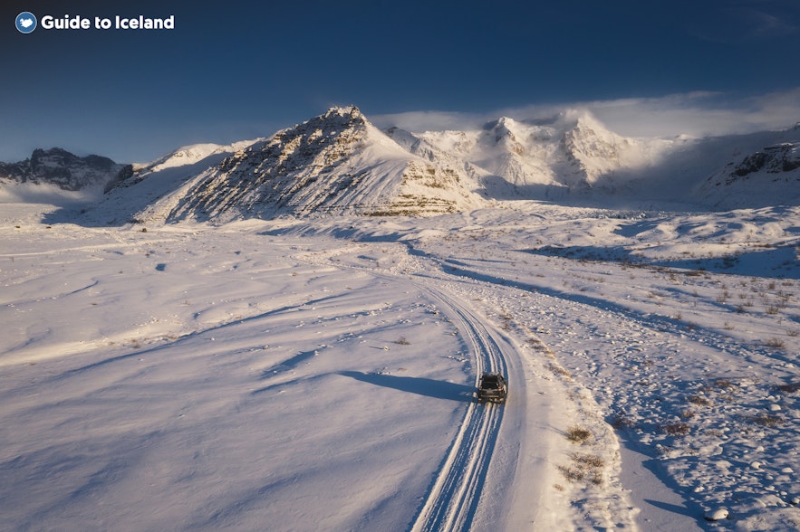 A car driving across a snow-covered East Iceland landscape during winter.