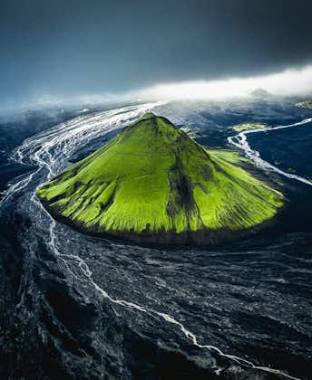 The bright green Maelifell volcano surrounded by black sands and river water.