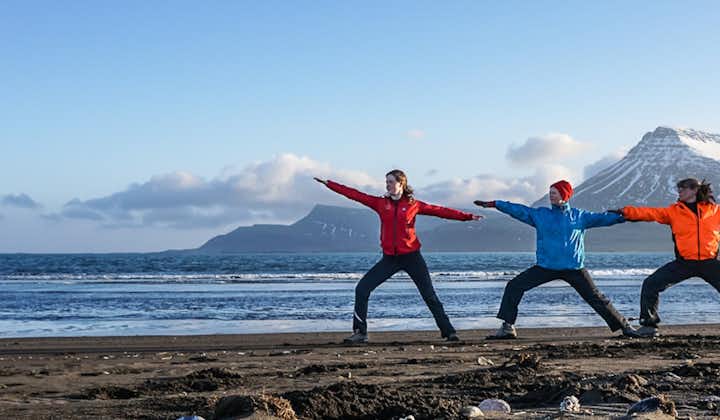 Travelers practicing mindfulness yoga on an Eastfjords black sand beach with snow-capped mountains behind.