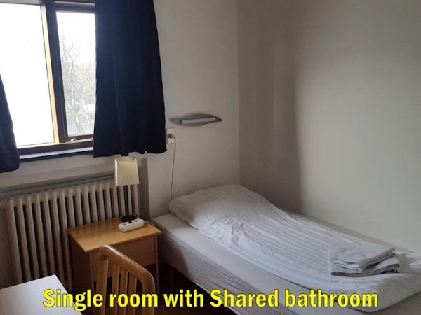 The single room with shared bathroom at Travel Inn Guesthouse with a nightstand and large window.