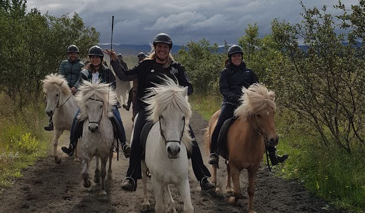 Happy riders traverse volcanic landscapes near Reykjavik, surrounded by gorgeous scenery of trees, grass, with hills in the distance and a cloudy sky above.