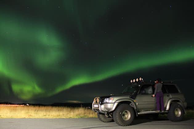 A super jeep with a woman standing on its ledge under the northern lights in Iceland.