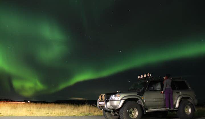 A super jeep with a woman standing on its ledge under the northern lights in Iceland.