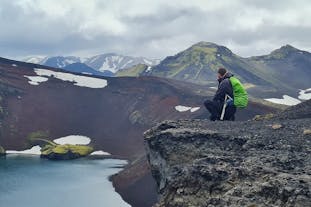 A man sits on a rock, overlooking a crater lake in the highlands of Iceland.