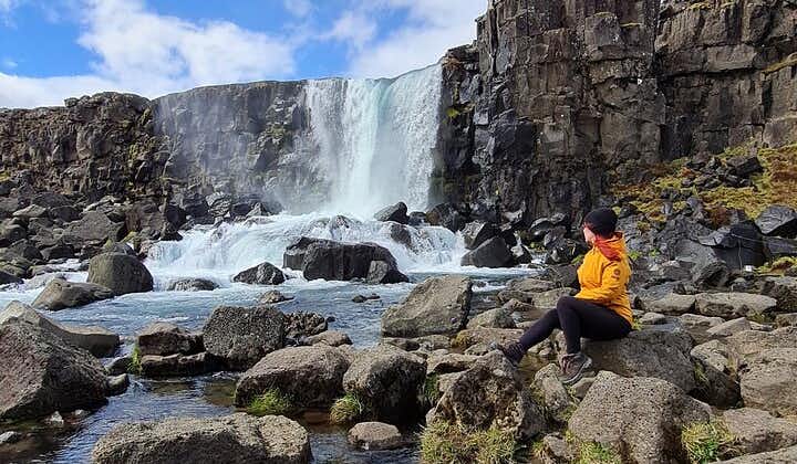 A person sits on the rocks surrounding the Oxararfoss waterfall in Thingvellir National Park.