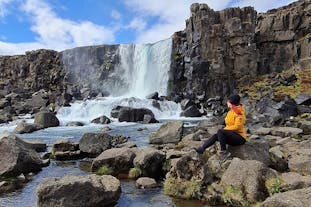 A person sits on the rocks surrounding the Oxararfoss waterfall in Thingvellir National Park.