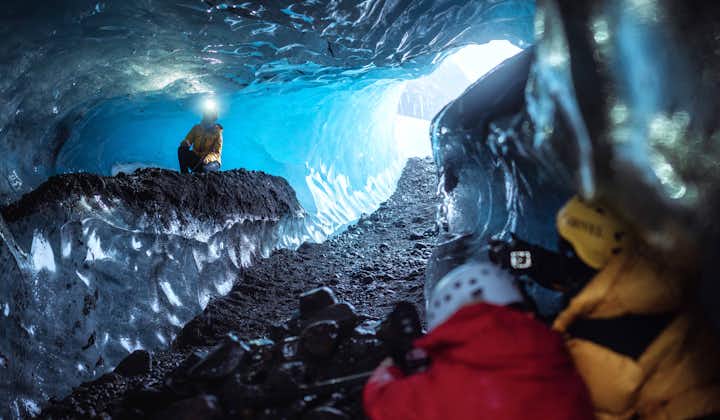 Two people take photos of another person wearing a head torch in an ice cave in Iceland.