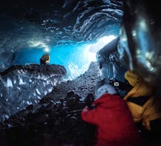 Two people take photos of another person wearing a head torch in an ice cave in Iceland.