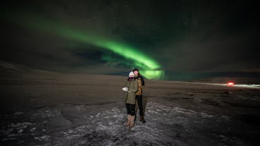 A couple poses for a photo with the beautiful northern lights as their backdrop.