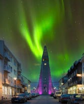 The Hallgrimskirkja church in Reykjavik with the northern lights shining green in the sky above it.