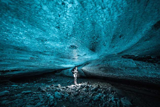 A person stands in an ice cave with a brilliant ceiling of blue ice overhead.