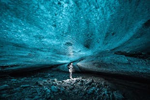 A person stands in an ice cave with a brilliant ceiling of blue ice overhead.