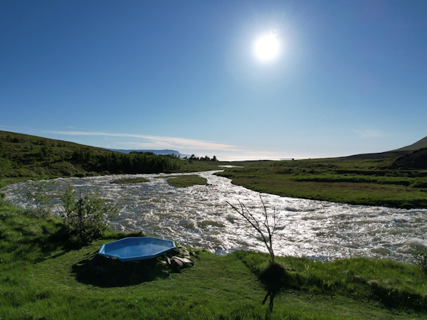 The modern jacuzzi at Dalasetur boasts an incredible setting amid nature, with a stream on one side and green pastures on the ot