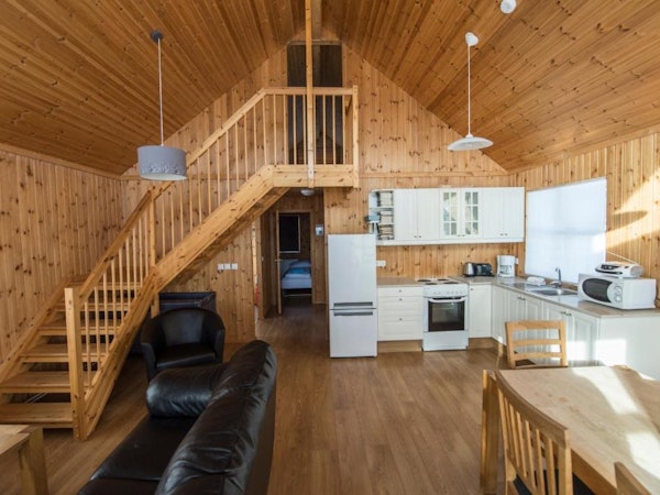 The open-plan living and dining area, and a kitchen with a wooden staircase at Gladheimar cottages.